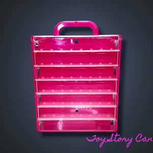 Peut inclure: Une boîte de rangement rose vif à compartiments multiples avec une poignée. Elle comporte plusieurs étagères horizontales transparentes. La boîte est conçue pour contenir de petits objets. Le fond est un dégradé gris foncé.