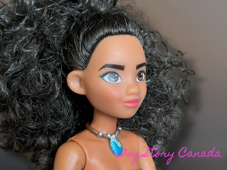 May include: A doll with dark skin, brown eyes, and black curly hair. The doll is wearing a necklace with a blue pendant. The doll's lips are pink, and it has a neutral expression. The doll is a character from a popular animated movie.