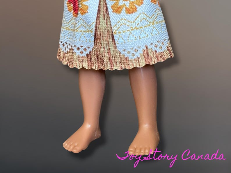 May include: A doll's legs and lower torso are visible, with a patterned skirt in shades of white, orange, and brown. The skirt has a scalloped edge. The doll's skin is a light tan color. The image is set against a gradient background.