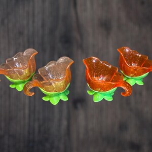 May include: Four orange plastic flower-shaped bowls with green stems. The bowls are designed to hold small items like jewellery or sweets.