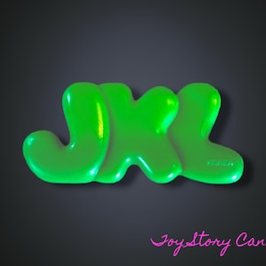 Puede incluir: Letras JXL de color verde brillante sobre un fondo gris oscuro. Las letras tienen un aspecto brillante y tridimensional. El texto "Joy Story Canada" está escrito en rosa en la parte inferior.