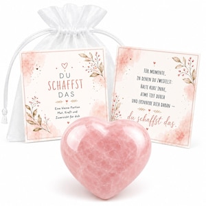 Könnte beinhalten: Ein polierter, herzförmiger rosa Stein steht vor zwei quadratischen Karten mit floralen Aquarell-Akzenten und deutschem Text, begleitet von einem weißen, transparenten Beutel mit Kordelzug. Die Karten enthalten die Aufschriften "Du schaffst das" und "Für Momente, in denen du zweifelst: Halte kurz inne, atme tief durch und erinnere dich daran - du schaffst das."