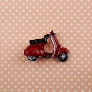 Könnte beinhalten: Ein roter Miniatur-Roller mit schwarzem Sitz und silbernen Akzenten. Der Roller befindet sich auf einem rosa-weißen Punktmuster-Hintergrund.