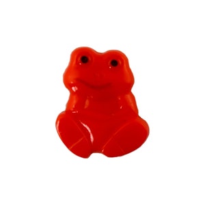 Könnte beinhalten: Ein knallroter Plastik-Froschknauf mit schwarzen Augen. Der Frosch sitzt mit gekreuzten Beinen.