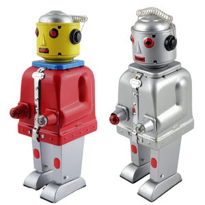Può includere: Due robot giocattolo retrò. Uno ha la testa gialla, il corpo rosso e le gambe argentate. L'altro è argentato con gli occhi rossi. Entrambi hanno un'antenna a molla e una luce rossa sul petto.