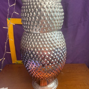 May include: A silver owl figurine with a textured, teardrop-shaped design. The owl is standing on a base with a decorative design.