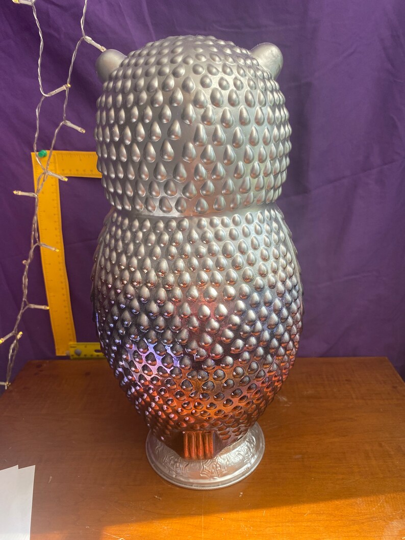 May include: A silver owl figurine with a textured, teardrop-shaped design. The owl is standing on a base with a decorative design.