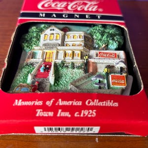 May include: A Coca-Cola brand magnet featuring a miniature replica of the Town Inn, c.1925, with a red staircase and green foliage. The magnet is in a red box with the Coca-Cola logo and the text "Memories of America Collectibles."
