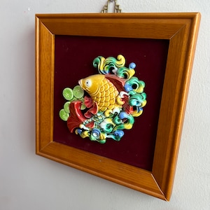 May include: A framed wall decor featuring a 3D ceramic fish with colorful details, set against a red velvet background.