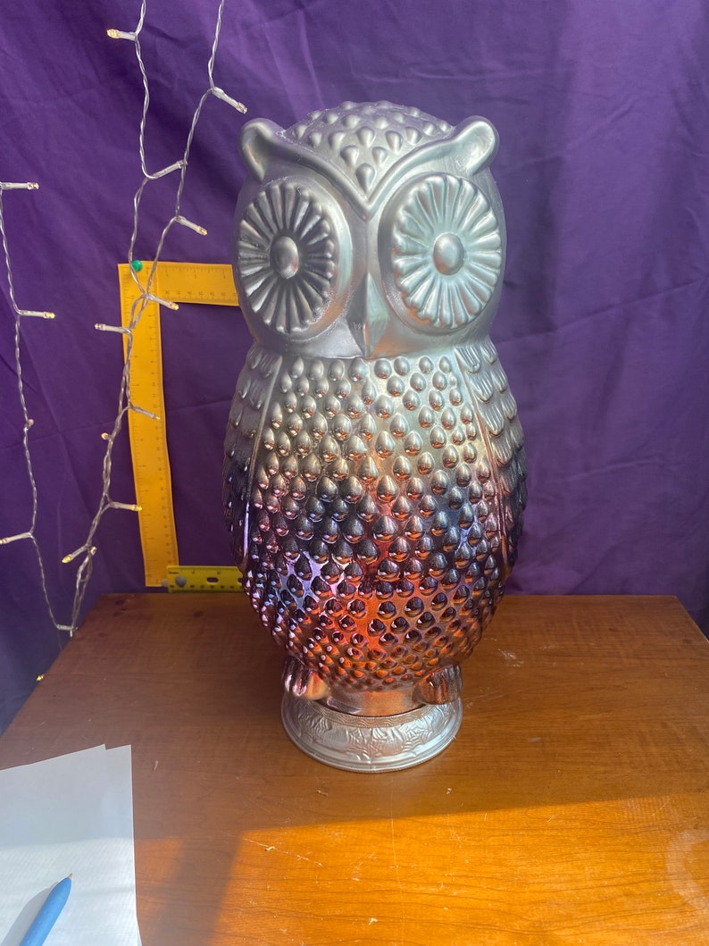May include: A silver and iridescent glass owl figurine with a textured surface. The owl has large, round eyes and a detailed beak.