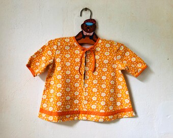 May include: Orange and white floral print baby dress with a zipper closure and a tie at the neck.