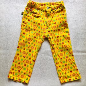 Op de afbeelding: Gele spijkerbroek met een patroon van rode tomaten, groene bladeren en gele wortels.