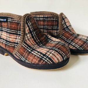 May include: A pair of brown plaid slippers with black trim and a black rubber sole. The slippers have the word "SUOMI" printed on the side.