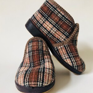 May include: A pair of brown and white checked slippers with a brown trim. The slippers have a dark brown rubber sole.