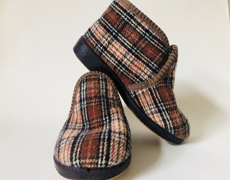 May include: A pair of brown and white checked slippers with a brown trim. The slippers have a dark brown rubber sole.