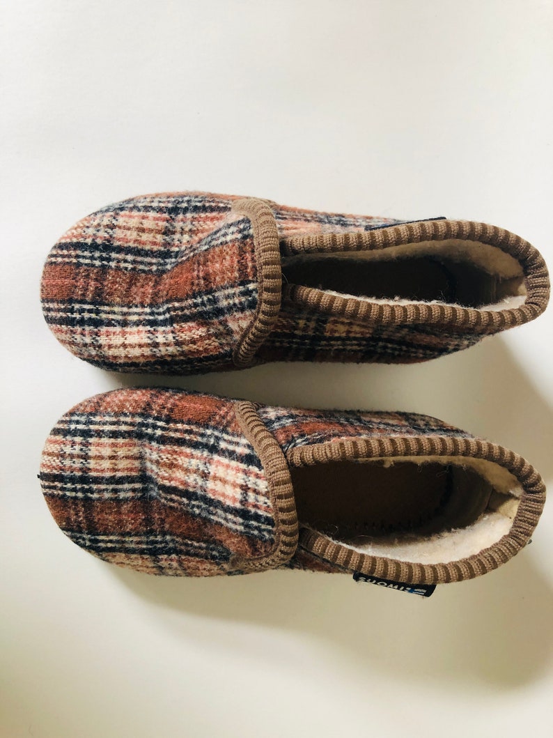 May include: A pair of brown and black plaid slippers with a brown fleece lining. The slippers have a brown elastic band at the top and the brand name "Simons" is visible on the bottom of one slipper.