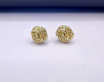 May include: A pair of gold knot-shaped earrings. The earrings are made of a textured metal and have a shiny finish.