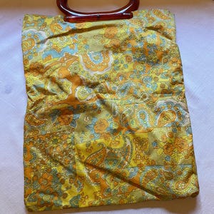 May include: A vintage yellow, orange and blue paisley patterned handbag with a brown plastic handle.