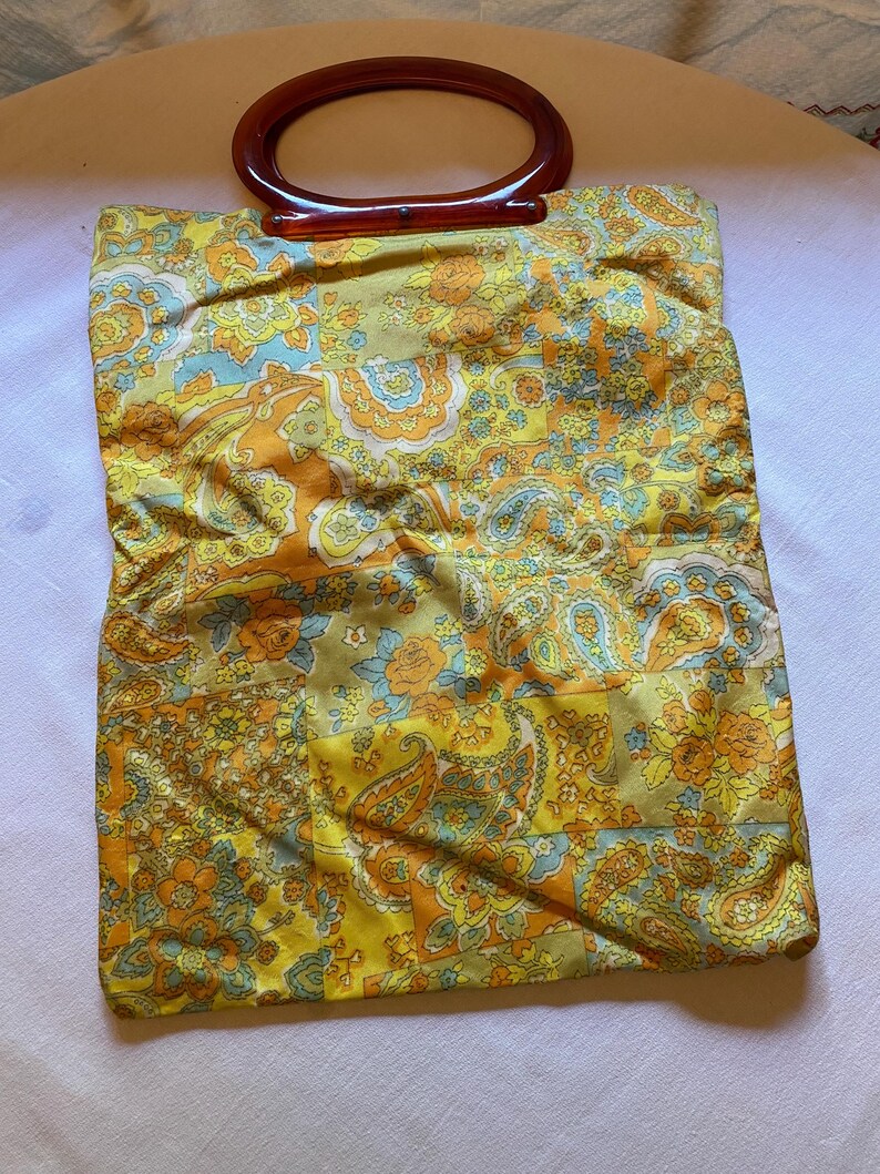 May include: A vintage yellow, orange and blue paisley patterned handbag with a brown plastic handle.