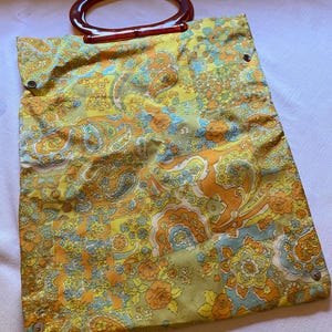 May include: A vintage yellow, orange and blue paisley patterned tote bag with a brown plastic handle.