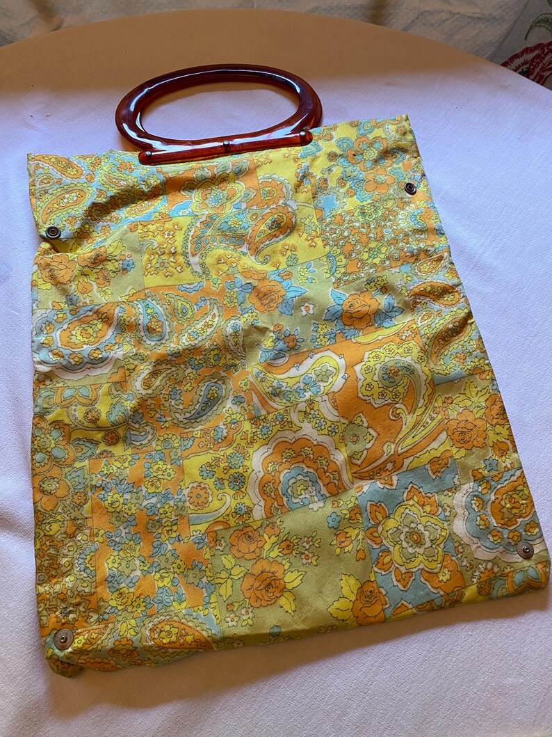 May include: A vintage yellow, orange and blue paisley patterned tote bag with a brown plastic handle.