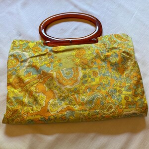 May include: A vintage yellow and orange paisley patterned handbag with a brown plastic handle.