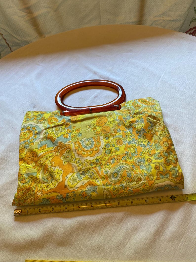 May include: A vintage yellow, orange and blue paisley patterned fabric handbag with a brown plastic handle.