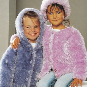 May include: Two children wearing fuzzy knit jackets. The girl on the left is wearing a blue jacket with a hood and the girl on the right is wearing a pink jacket. Both girls are wearing jeans.