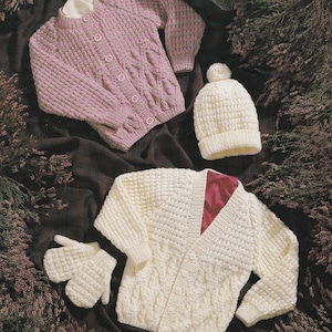 Peut inclure: Ensemble de vêtements pour enfants tricotés dans des tons pastel. L'image présente un cardigan boutonné violet clair, un bonnet crème avec un pompon, un cardigan crème et des mitaines assorties. Les vêtements sont disposés sur un fond sombre à motifs.