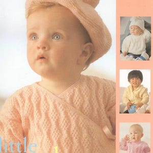 May include: A pink knitted baby sweater with a wrap-around style and a matching pink knitted hat with pom-poms. The image includes the text "little angels".