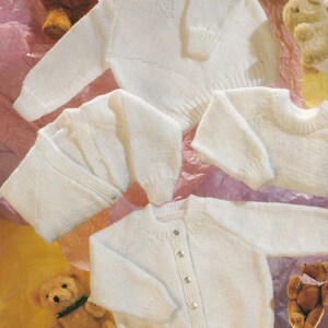 May include: Three white knitted baby sweaters, one with a V-neck, one with a round neck, and one with a button-up front.