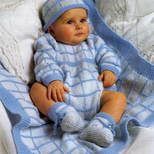 Könnte beinhalten: Ein Baby in einem hellblau-weißen Strick-Set, bestehend aus Mütze, Strampler und Babyschuhen. Das Set hat ein Gittermuster. Das Baby sitzt auf einer passenden Decke mit blauem Rand.