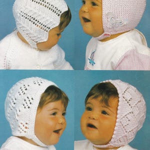 Op de afbeelding: Twee baby's dragen gebreide baby mutsen met oorflappen. Eén muts is wit met een kantpatroon en de andere is roze met een vlinderversiering.