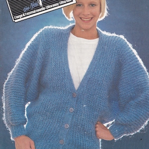May include: A blue knitted cardigan with a V-neck and button closure. The cardigan has a textured knit pattern and is worn by a person with short blonde hair. The text "the New Knitting idea" is visible in the top left corner of the image.