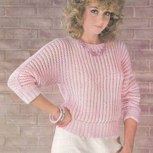 Könnte beinhalten: Ein rosa gestrickter Pullover mit lockerer Passform und gerippter Struktur. Der Pullover hat einen runden Ausschnitt und lange Ärmel.