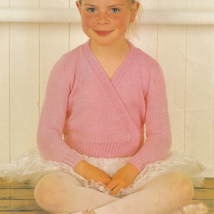 May include: A light pink ballet wrap sweater with long sleeves. The sweater is worn over a white tutu skirt. The ballet outfit is completed with ballet shoes and tights. The outfit is designed for a young dancer.