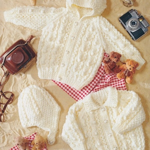 May include: Two white crocheted baby cardigans with button fastenings. One cardigan has a hood and the other has a collar. Both cardigans feature a textured, bobbly design.