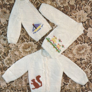 May include: Three white knitted baby cardigans with different embroidered designs. One cardigan features a sailboat, another has a row of birds, and the third has a squirrel.