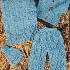 Puede incluir: Un conjunto de ropa de punto azul para bebé que incluye un gorro, un cárdigan y unos pantalones. El conjunto presenta un patrón de punto de cable.