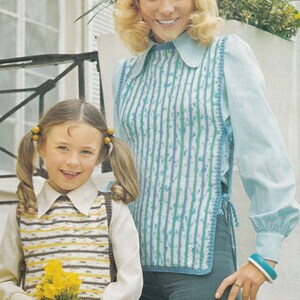 May include: Two people wearing knitted vests over collared shirts. The vests have vertical stripes in blue, white, and yellow. One person holds a bouquet of yellow flowers. The background includes a white wall and a window.