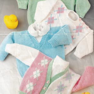 Puede incluir: Tres jerséis de punto para bebé en diferentes colores y patrones. Los jerséis están hechos con hilo blanco y presentan una combinación de colores rosa, verde y azul. Los jerséis tienen un patrón de rombos con un diseño de copo de nieve.
