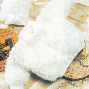 Op de afbeelding: Witte gebreide baby-cardigan en bijpassende slofjes met een textuur, fluffy ontwerp. De cardigan heeft een knoopsluiting en een V-hals.