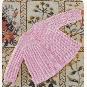 May include: A pink knitted baby cardigan with a button fastening. The cardigan is made with a textured stitch pattern.