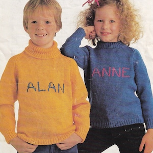 May include: Two children wearing yellow and blue knitted sweaters with their names, "ALAN" and "ANNE", embroidered on the front.