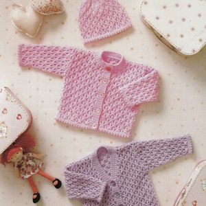 Könnte beinhalten: Ein hellrosa Baby-Strickjacke mit passendem Hut, beide mit offenem Gewebe. Die Strickjacke hat eine Knopfleiste vorne und ein strukturiertes Muster. Eine zweite lavendelfarbene Strickjacke ist ebenfalls zu sehen. Dekorative Accessoires sind ebenfalls vorhanden.