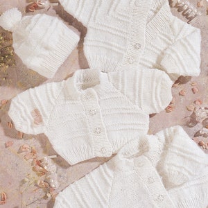 Op de afbeelding: Drie witte gebreide baby-vestjes en een witte gebreide baby-muts met een pompon. De vestjes zijn aan de voorkant geknoopt en hebben een geribbelde textuur. Het label "PREMATURE" is zichtbaar in de rechterbovenhoek van de afbeelding.