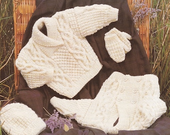 May include: A set of knitted baby clothes in a cream color, including a sweater, pants, hat, and mittens. The clothes are laid out on a brown plaid fabric.