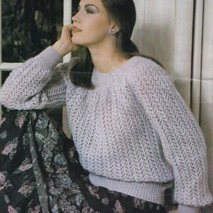 May include: A light purple knitted jumper with a delicate open stitch pattern. The jumper has a round neckline and long sleeves.