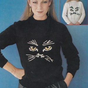 May include: A black sweater with a white embroidered cat face on the front. The cat face has yellow eyes and white whiskers. The sweater is being modeled by a woman with long blonde hair.