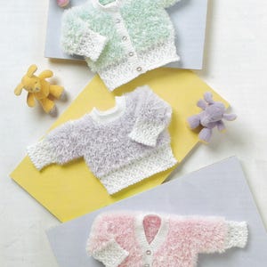 Puede incluir: Tres cárdigans de bebé esponjosos en colores pastel: verde menta, lavanda y rosa. Cada suéter tiene un ribete de ganchillo blanco y cierre de botón. Pequeños peluches de colores coordinados están esparcidos alrededor de los suéteres.